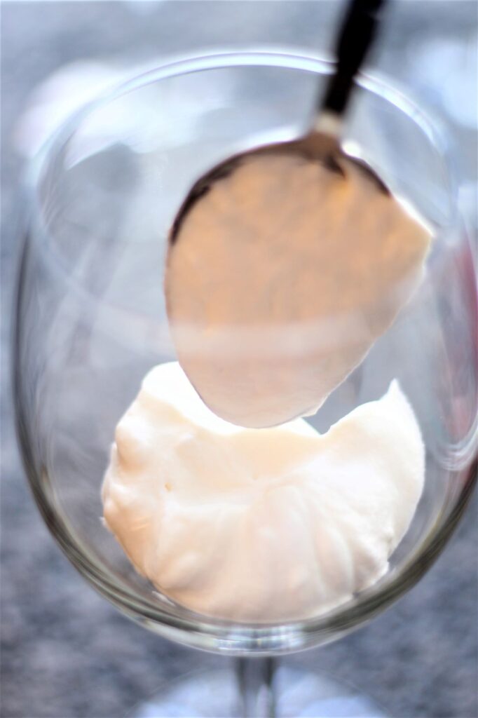 putting a dollop of whipped cream into bottom of wine glass