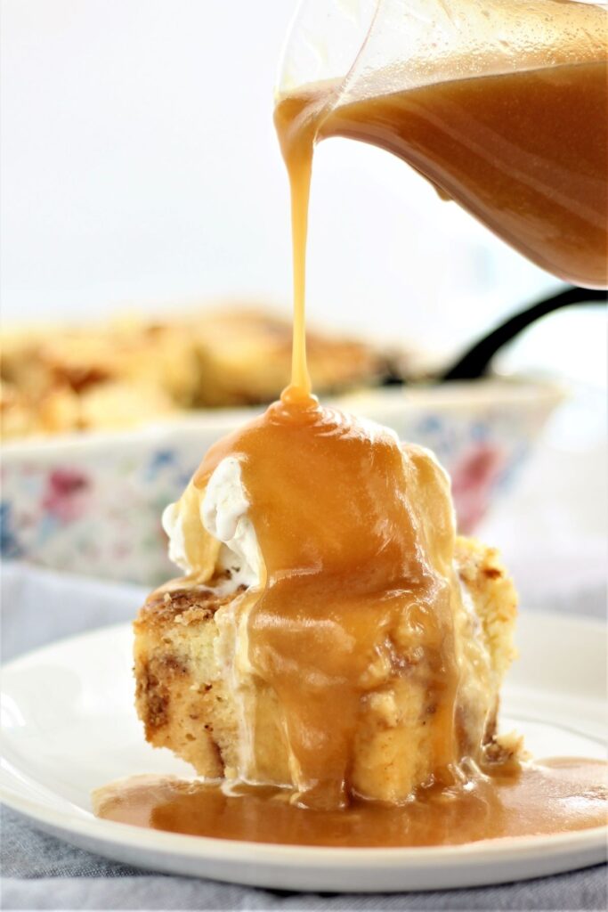 pouring butter rum sauce over bread pudding on white plate