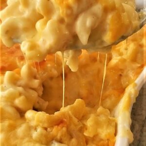 lifting spoonful of baked mac and cheese out of white casserole dish