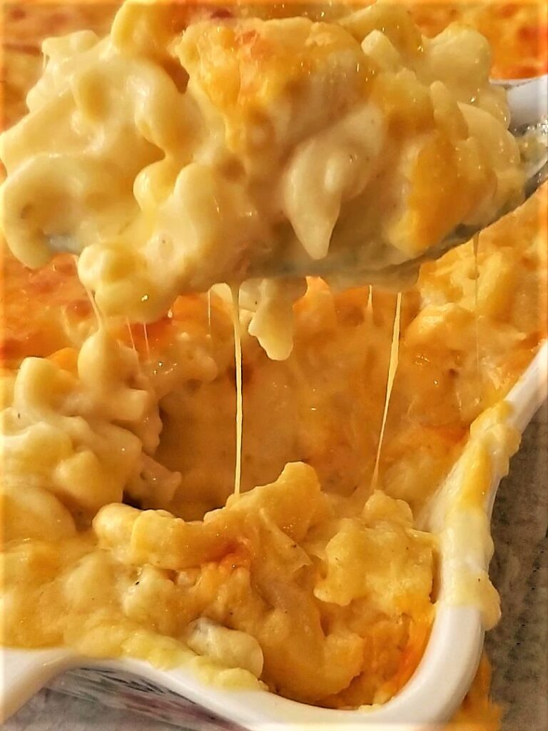 lifting spoonful of baked mac and cheese out of white casserole dish