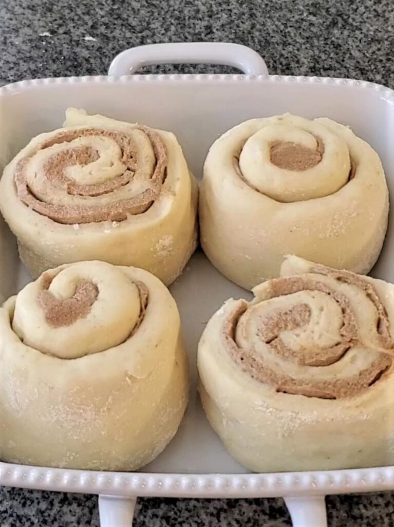 four risen cinnamon rolls in white baking pan