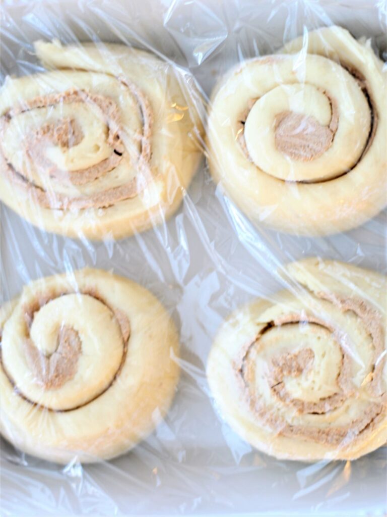 covering rolls in white baking pan with plastic wrap