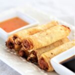 stacked gluten free lumpia on white platter with two sauces