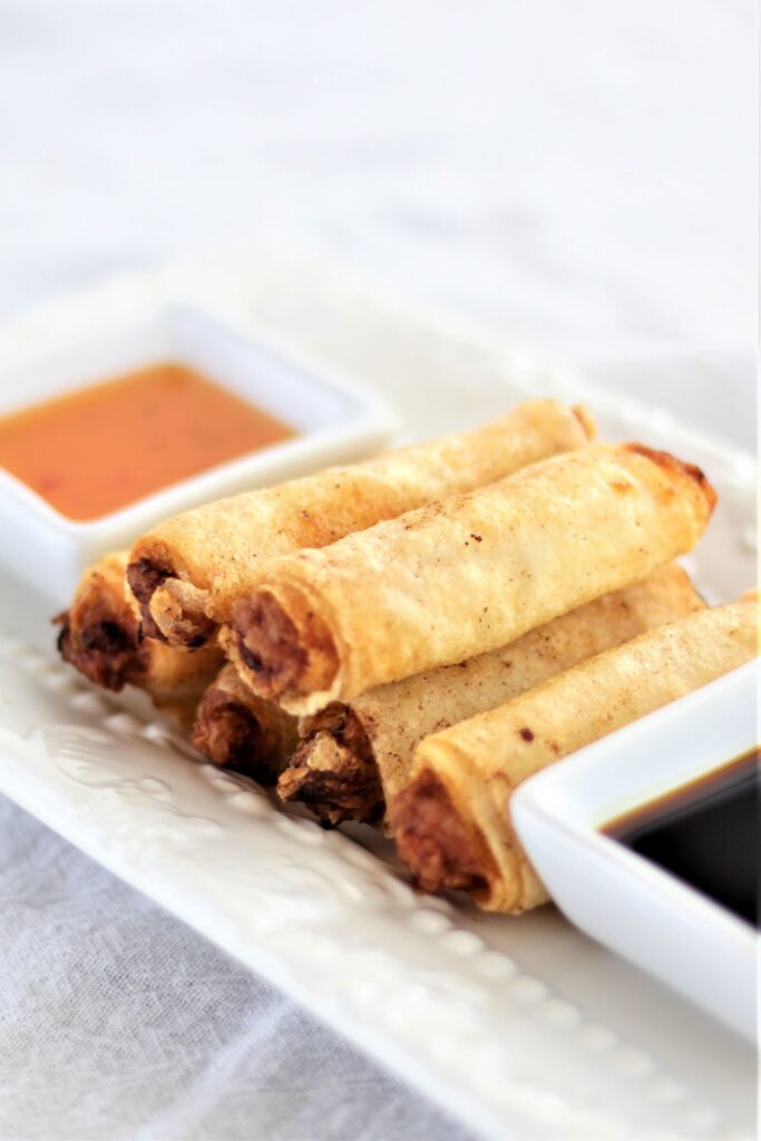 stacked gluten free lumpia on white platter with two sauces