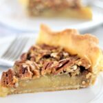 piece of gluten free pecan pie on white plate with another piece in the background