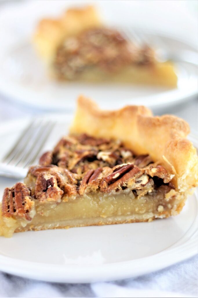 piece of gluten free pecan pie on white plate with another piece in the background