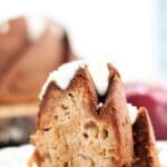 slice of gluten free apple bundt cake on white plate with red apple in background