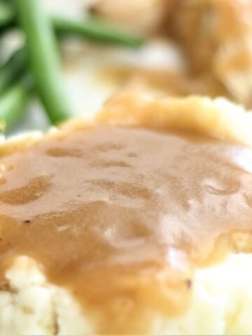 landscape view of mashed potatoes covered in gravy, green beans, and sliced turkey on white plate