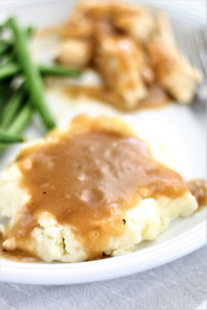 mashed potatoes with turkey gravy, green beans, and turkey on white plate
