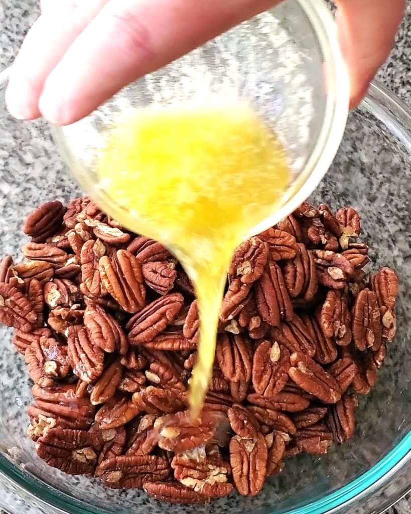 pouring melted butter onto pecans