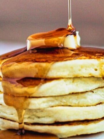 landscape view of a stack of gf pancakes on a colorful plate with butter on top and syrup pouring over.