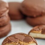 cut open gluten free tagalong cookie on white plate with stacks of unopened cookies