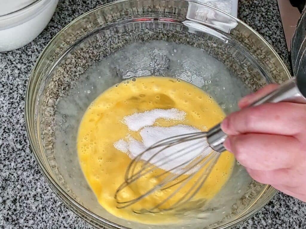 whisking eggs with sugar in large glass bowl.