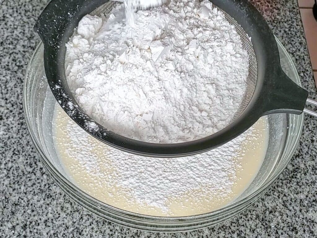 sifting dry ingredients over wet ingredients in bowl.