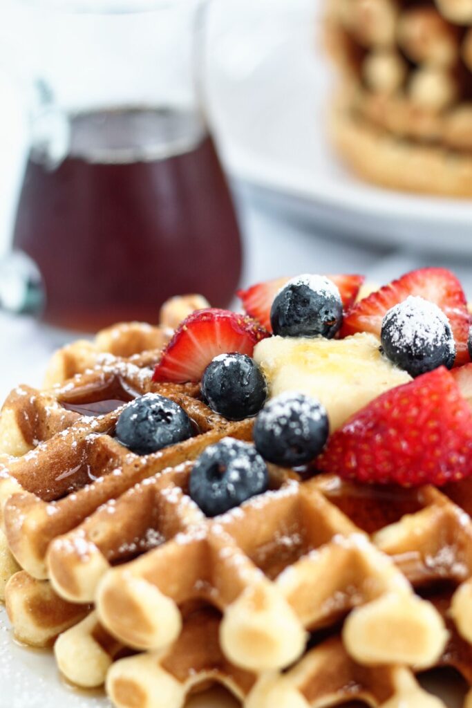 two mochi waffles stacked on white plate with berries and syrup on top