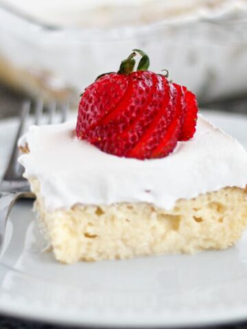 landscape view of slice of tres leches cake on white plate with fanned strawberry on top