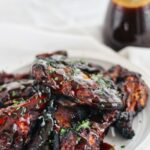 gluten free honey coriander wings on a white plate with sauce in the background