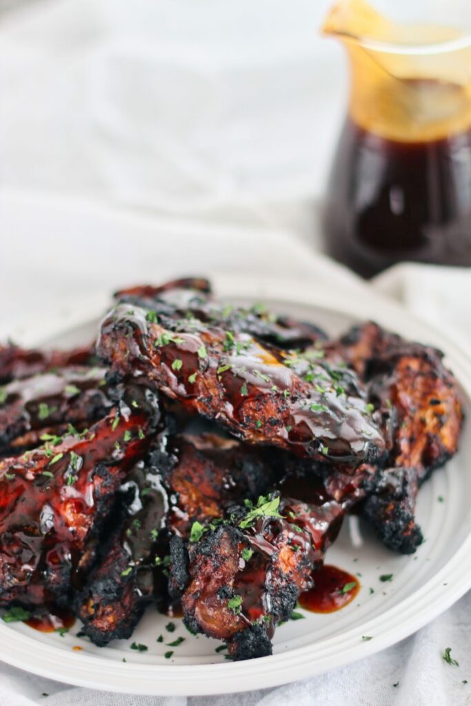 gluten free honey coriander wings on a white plate with sauce in the background