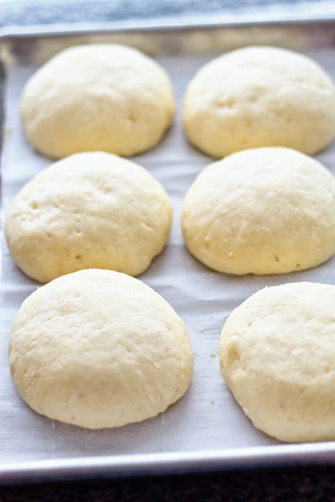proofed buns ready for the oven on parchment-lined baking sheet