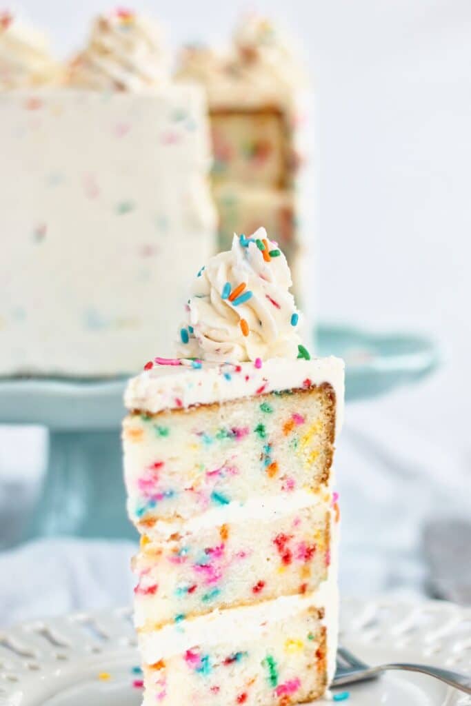 slice of cake on white plate with whole cake on blue cake stand behind it