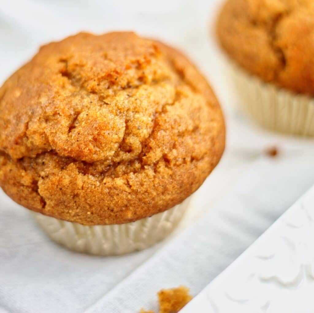 gluten free pumpkin muffins in gold wrappers and crumbs on white towel.