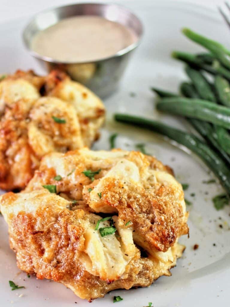 two crab cakes on white plate with green beans and a side of remoulade sauce