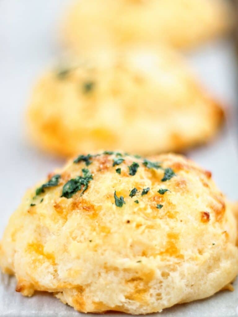 up close shot of three cheddar bay biscuits on white parchment-lined baking sheet.