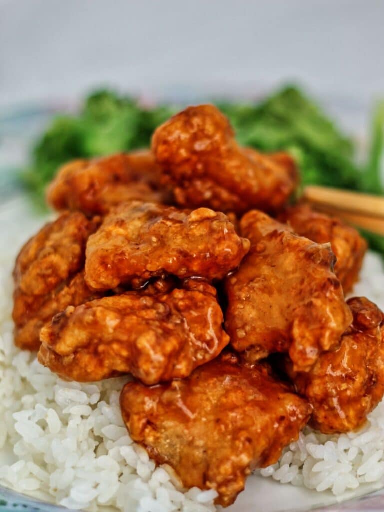 general tso's chicken on white rice with broccoli in the background.