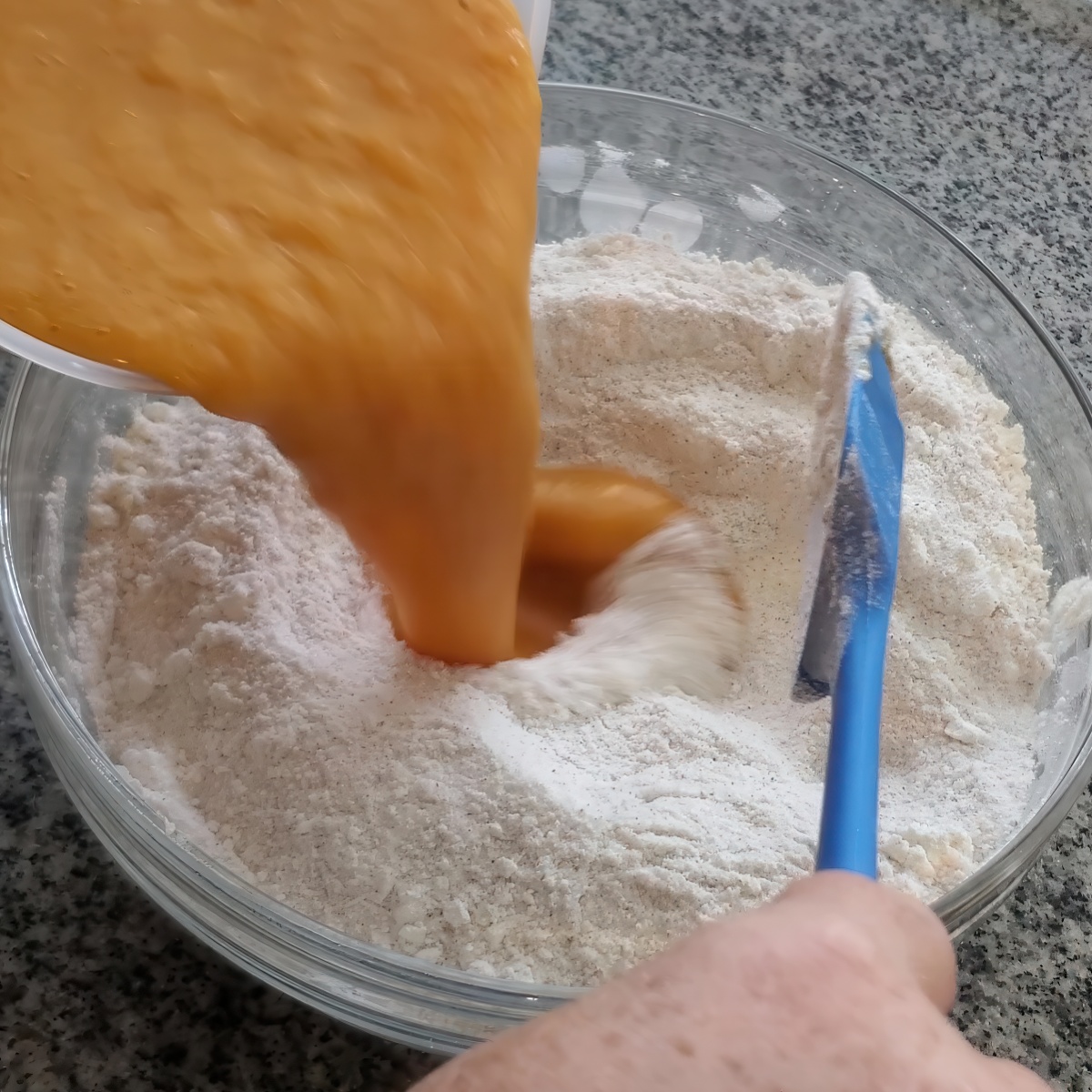 pouring pumpkin mixture into dry ingredients in glass bowl.