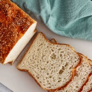 half sliced loaf of gluten free English muffin bread on white cutting board with teal cloth napkin.