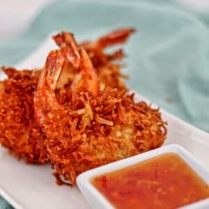 three gf coconut shrimp on white rectangular plate with small white square bowl with orange dipping sauce.