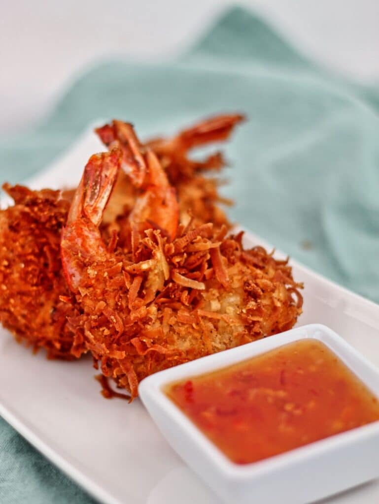 three gf coconut shrimp on white rectangular plate with small white square bowl with orange dipping sauce.