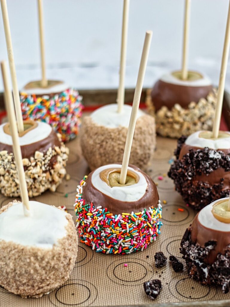 caramel apples on silicone-lined baking sheet with several different toppings.