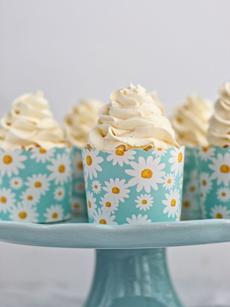 several vanilla cupcakes in daisy cardboard cupcake liners on robin's egg blue cake stand.