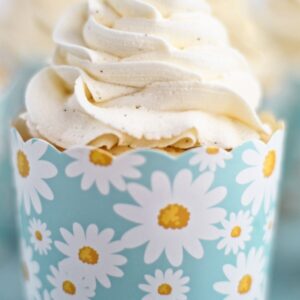 close up of vanilla cupcake in daisy cardboard wrapper with a blue background.