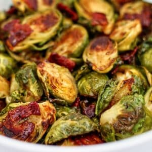 roasted brussels sprouts with cider glaze and bacon in large white bowl.
