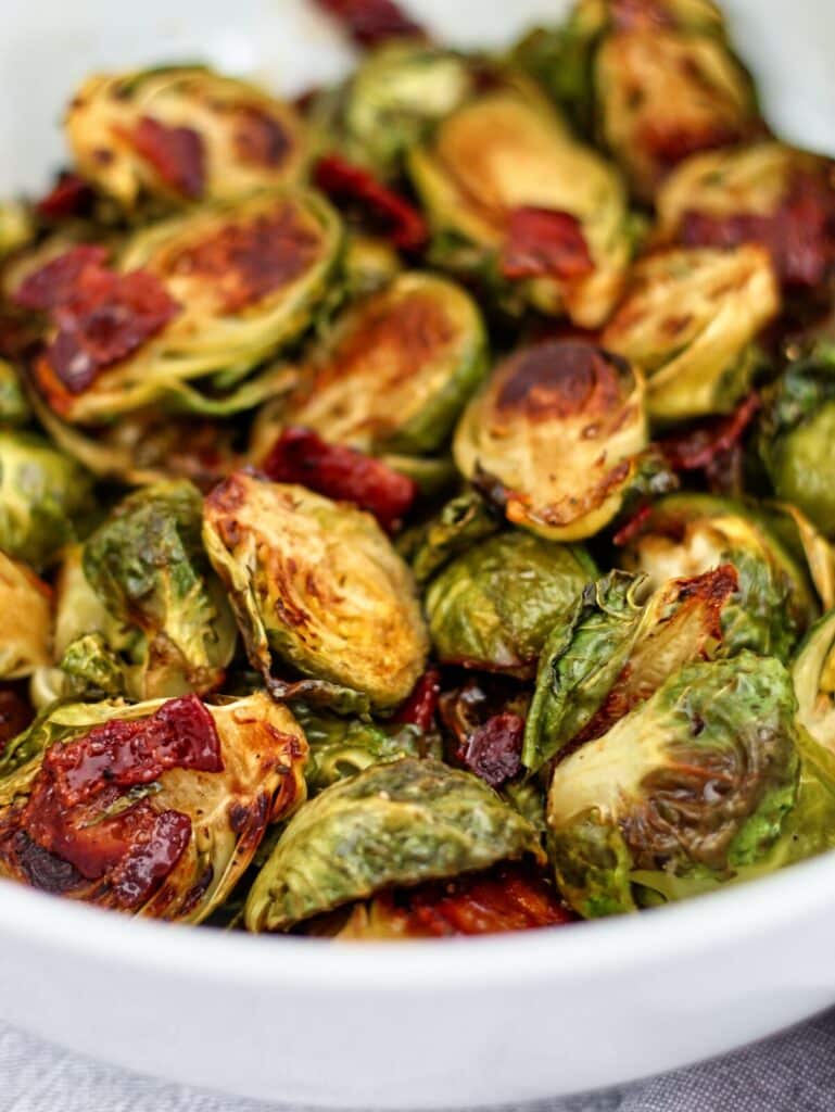 roasted brussels sprouts with cider glaze and bacon in large white bowl.