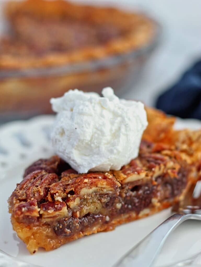 slice of gf chocolate pecan pie on white plate with whole pie in the background.