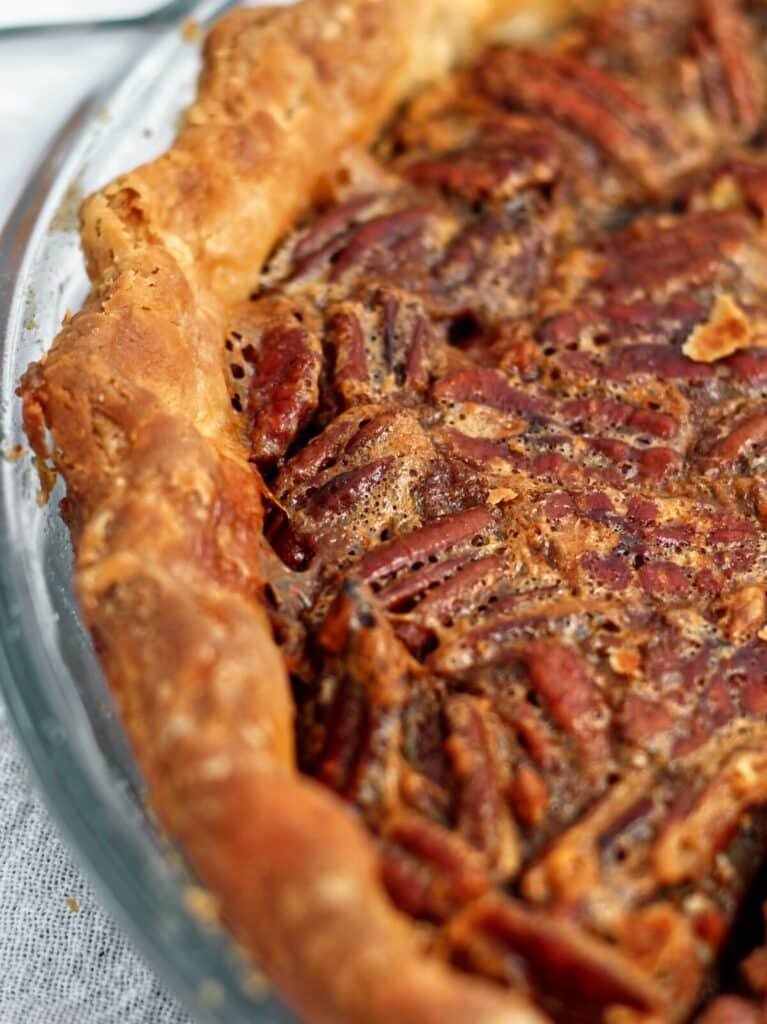 close up shot of one side of whole chocolate pecan pie in glass pie plate.
