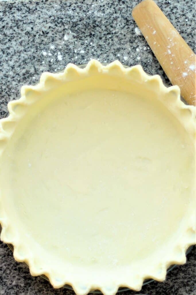 unbaked gluten free buttery pie crust in pie pan with wooden French rolling pin beside it.