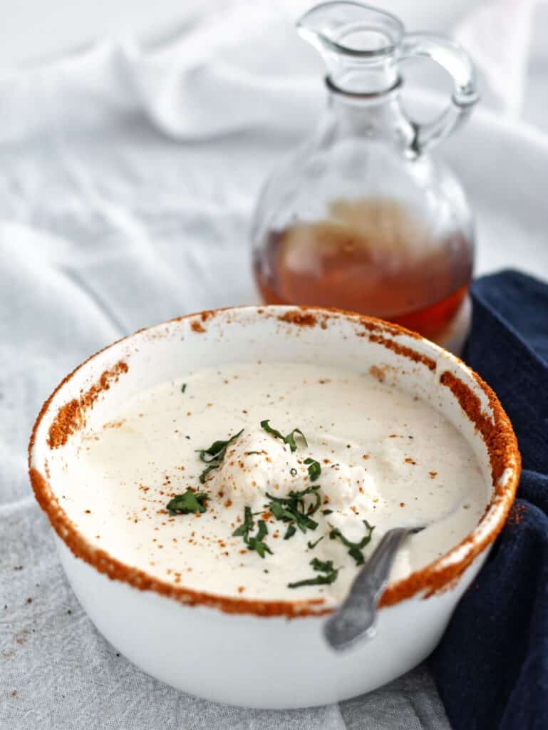 bowl of she crab soup on white linen with navy blue linen napkin beside it and glass bottle of sherry behind it.