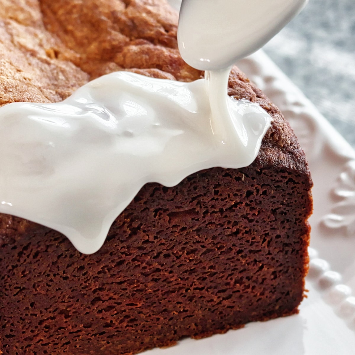 pouring thick white glaze over top and down sides of lemon loaf cake.