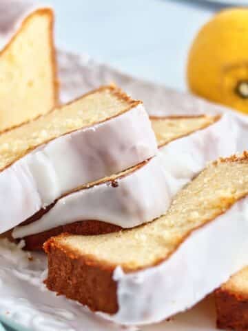 slices of lemon loaf cake on white platter with lemon in the background.