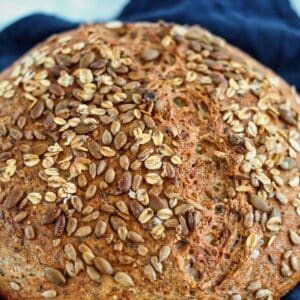 whole round loaf of multigrain bread on navy blue cloth napkin.