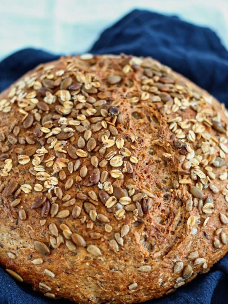 whole round loaf of multigrain bread on navy blue cloth napkin.