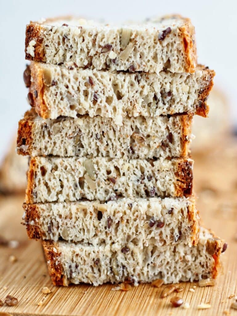 cut slices of gluten free seeded bread stacked on cutting board.