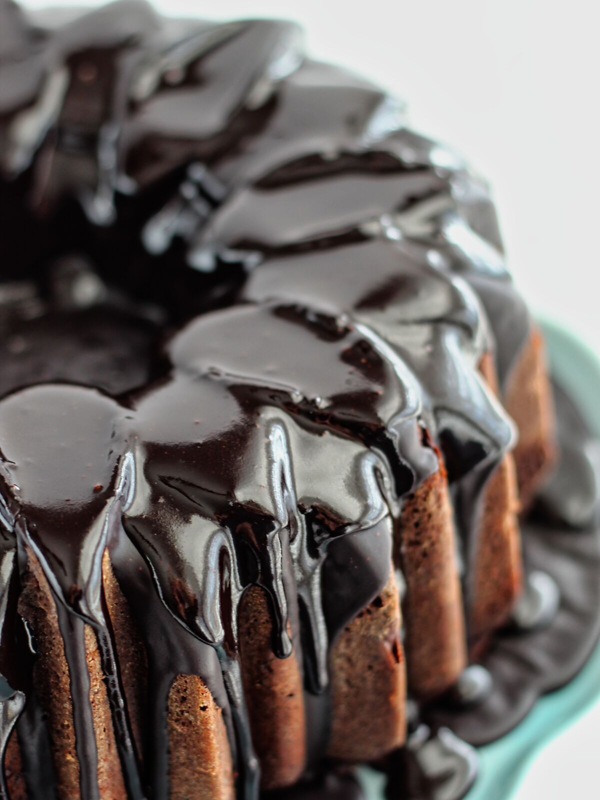 half moon of chocolate fudge bundt cake on blue cake stand dripping with chocolate fudge icing.