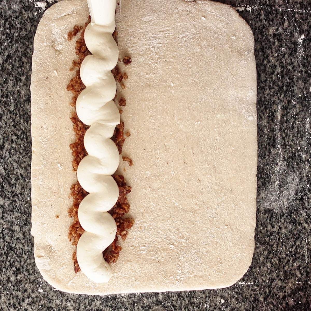 piping the cream cheese filling on top of the praline filling on the rectangle of dough.