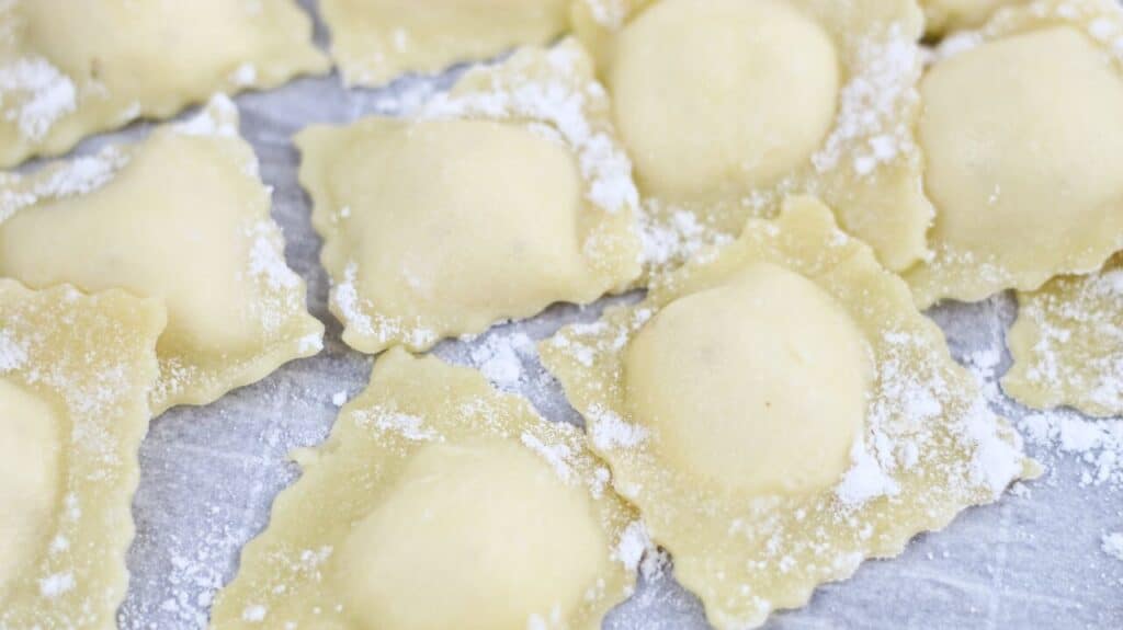 uncooked cheese ravioli on a sheet of parchment paper.