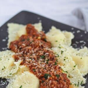 gluten free cheese ravioli on black square plate with red meat sauce on top.